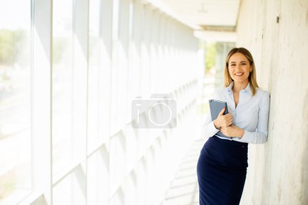 Téléchargez les photos : Jolie jeune femme d'affaires tenant avec ordinateur portable dans le couloir du bureau - en image libre de droit