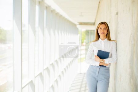 Foto de Mujer de negocios bastante joven sosteniendo con cuaderno en el pasillo de la oficina - Imagen libre de derechos