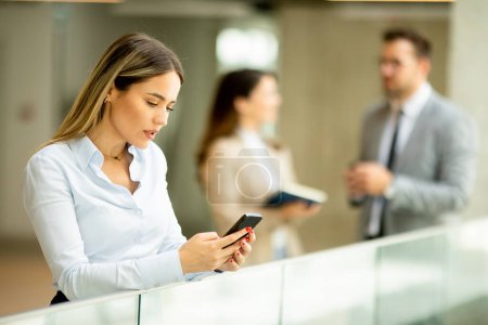 Photo for Young business woman standing with mobile phone in the office hallway - Royalty Free Image
