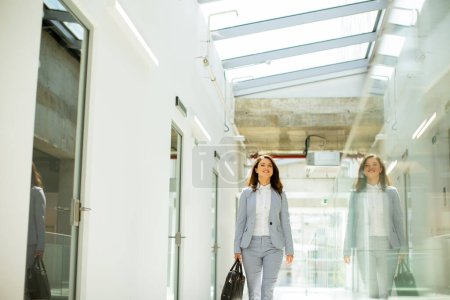 Photo for Pretty young business woman walking with briefcase in office hallway - Royalty Free Image