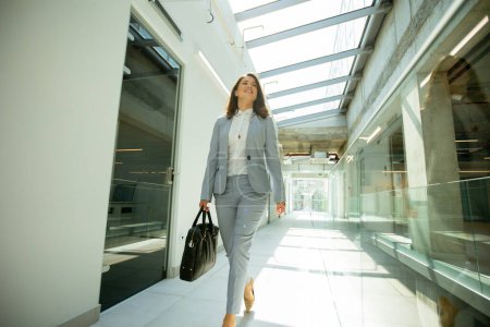 Photo for Pretty young business woman walking with briefcase in office hallway - Royalty Free Image