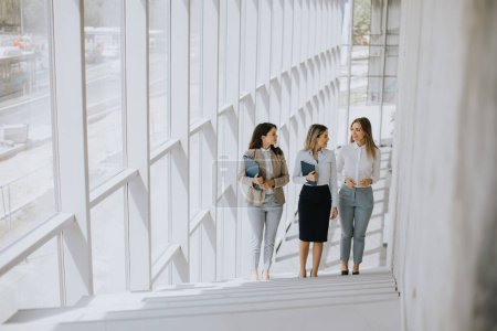 Photo for Three cute young business women walking on stairs in the office hallway - Royalty Free Image