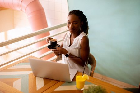 Photo for Pretty young black woman drinking coffee while working on laptop in the cafe - Royalty Free Image
