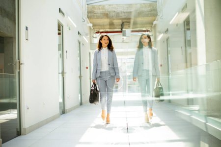 Téléchargez les photos : Jolie jeune femme d'affaires marchant avec mallette dans le couloir du bureau - en image libre de droit
