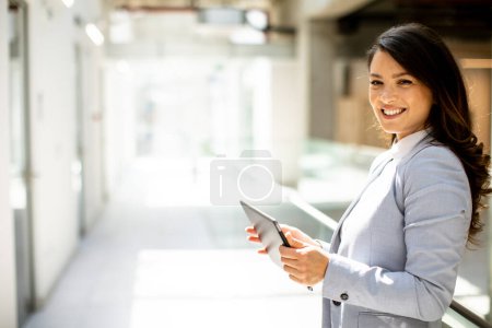 Téléchargez les photos : Jolie jeune femme travaillant sur tablette numérique dans le couloir du bureau - en image libre de droit
