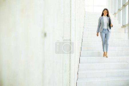 Téléchargez les photos : Jeune femme d'affaires marchant dans les escaliers et tenant un ordinateur portable dans le couloir du bureau - en image libre de droit