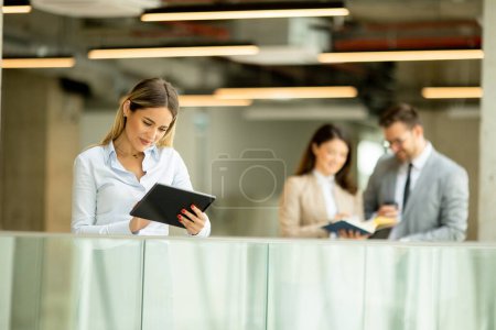 Téléchargez les photos : Jeune femme d'affaires debout avec tablette numérique dans le couloir du bureau - en image libre de droit