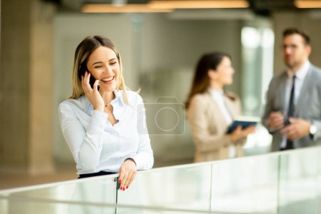 Téléchargez les photos : Jeune femme d'affaires debout avec téléphone portable dans le couloir du bureau - en image libre de droit