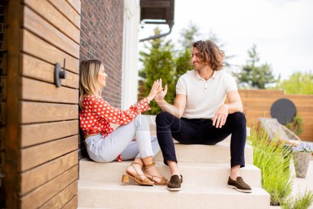 Téléchargez les photos : Beau jeune couple souriant amoureux assis devant la maison - en image libre de droit