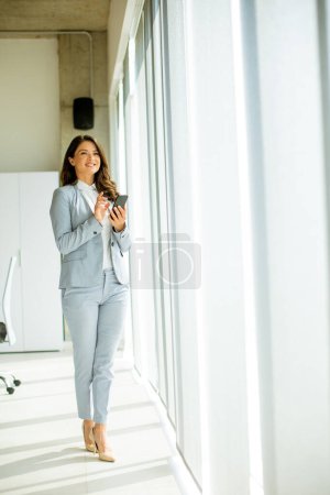 Foto de Mujer bastante joven usando el teléfono móvil junto a la ventana de la oficina - Imagen libre de derechos