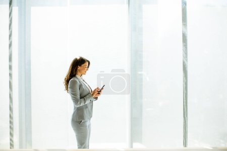 Photo for Pretty young woman using mobile phone by the office window - Royalty Free Image