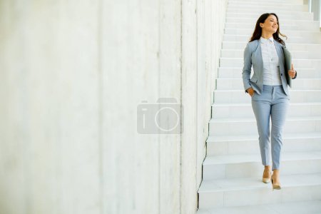 Foto de Joven mujer de negocios bajando las escaleras y sosteniendo el portátil en el pasillo de la oficina - Imagen libre de derechos