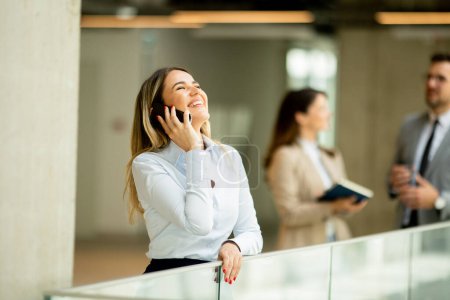 Téléchargez les photos : Jeune femme d'affaires debout avec téléphone portable dans le couloir du bureau - en image libre de droit