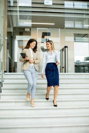 Foto de Dos mujeres de negocios jóvenes lindos caminando por las escaleras en el pasillo de la oficina - Imagen libre de derechos