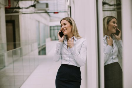 Photo for Pretty young business woman using mobile phone in the office hallway - Royalty Free Image