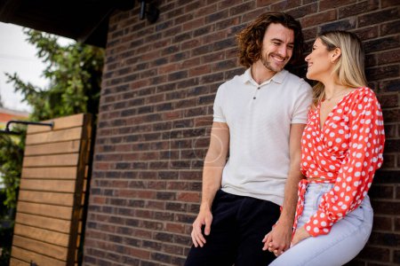Téléchargez les photos : Beau jeune couple souriant amoureux debout devant le mur de briques de la maison - en image libre de droit