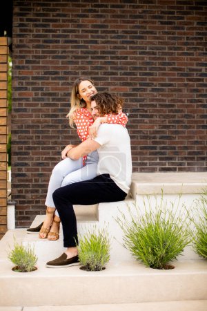 Photo for Handsome ymiling young couple in love sitting in front of house brick wall - Royalty Free Image