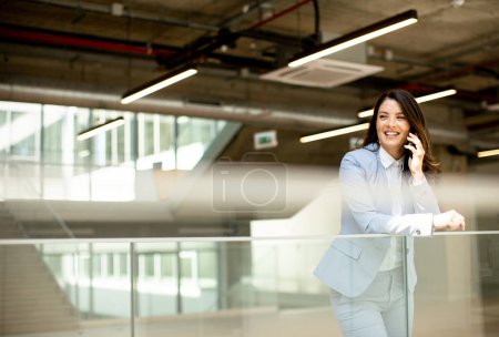 Photo for Pretty young business woman using mobile phone in the office hallway - Royalty Free Image