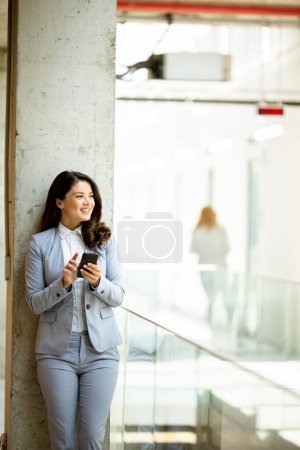 Téléchargez les photos : Jolie jeune femme d'affaires utilisant un téléphone portable dans le couloir du bureau - en image libre de droit