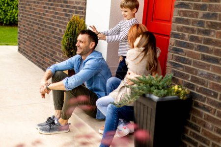Foto de Familia con una madre, padre, hijo e hija sentados fuera en las escaleras de un porche delantero de una casa de ladrillo - Imagen libre de derechos