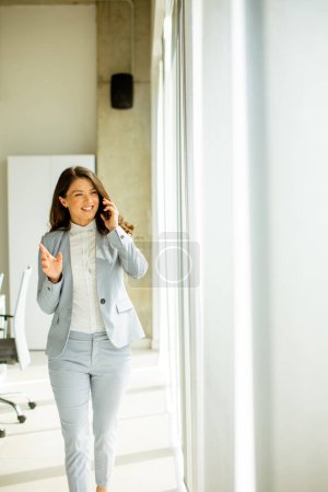 Photo for Pretty young woman using mobile phone by the office window - Royalty Free Image