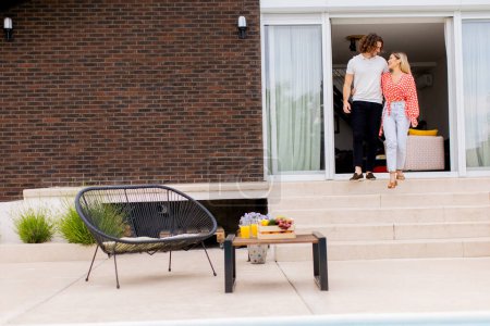 Téléchargez les photos : Beau jeune couple marchant dans les escaliers près de la piscine dans la cour arrière de la maison - en image libre de droit
