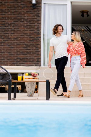 Téléchargez les photos : Beau jeune couple marchant dans les escaliers près de la piscine dans la cour arrière de la maison - en image libre de droit