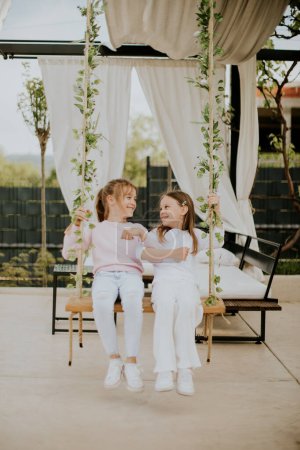 Téléchargez les photos : Deux jolies petites filles sur la balançoire dans le jardin de la maison - en image libre de droit