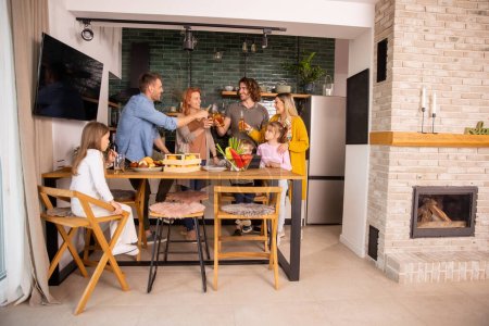 Téléchargez les photos : Deux familles heureuses trinquent au cidre tout en préparant le dîner dans la cuisine - en image libre de droit