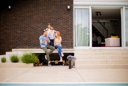 Photo for Family with a mother, father, son and daughter sitting outside by the swimming pool and eating strawberries - Royalty Free Image