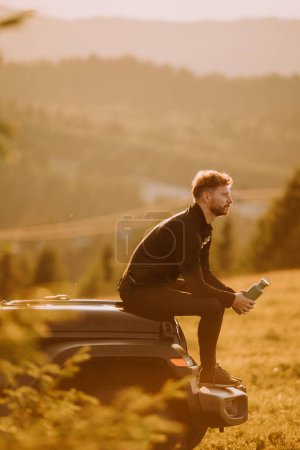 Téléchargez les photos : Handsome young man relaxing on a terrain vehicle hood at countryside - en image libre de droit