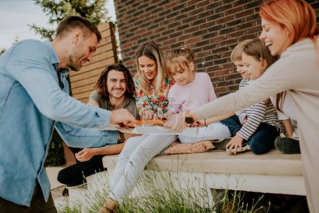 Téléchargez les photos : Heureux groupe de jeunes et d'enfants mangeant de la pizza dans la cour arrière de la maison - en image libre de droit