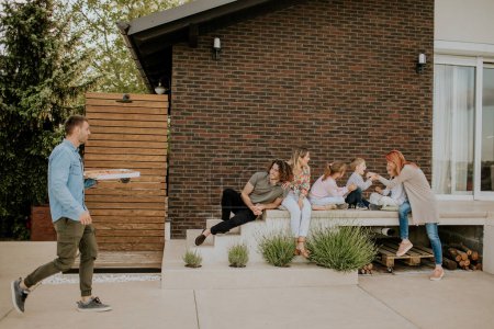Téléchargez les photos : Heureux groupe de jeunes et d'enfants se préparant à manger de la pizza dans la cour arrière de la maison - en image libre de droit