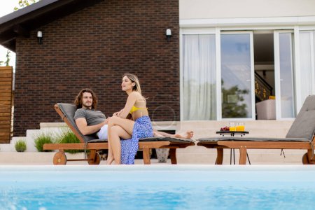Téléchargez les photos : Beau jeune couple relaxant au bord de la piscine dans la maison arrière-cour - en image libre de droit