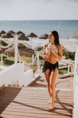 Foto de Mujer joven sonriente en bikini disfrutando de vacaciones en la playa mientras bebe cóctel - Imagen libre de derechos