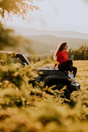 Photo for Pretty young woman relaxing on a terrain vehicle hood at countryside - Royalty Free Image
