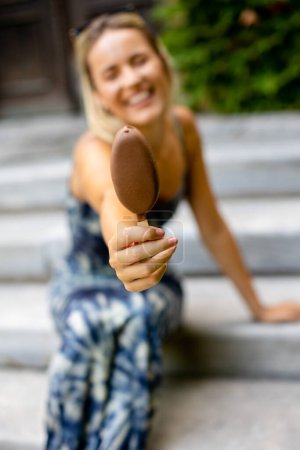 Téléchargez les photos : Jolie jeune femme assise dans les escaliers et mangeant de la crème glacée sur bâton - en image libre de droit