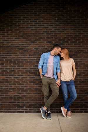Téléchargez les photos : Beau jeune couple souriant amoureux devant le mur de briques de la maison - en image libre de droit
