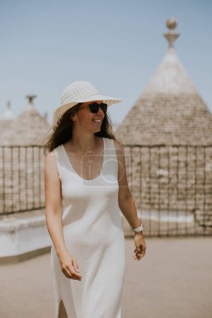 Téléchargez les photos : Une jeune femme en robe blanche et chapeau par une journée ensoleillée lors d'une visite touristique à Alborebello, Italie - en image libre de droit