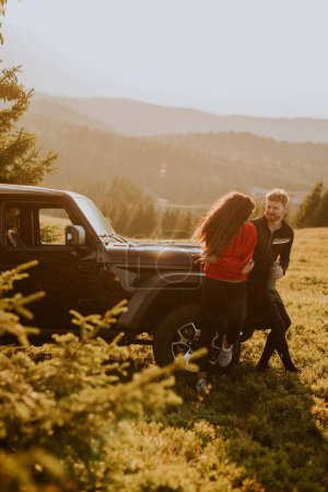 Téléchargez les photos : Handsome young couple relaxing by a terrain vehicle hood at countryside - en image libre de droit