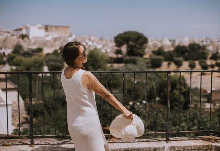Téléchargez les photos : Une jeune femme en robe blanche et chapeau par une journée ensoleillée lors d'une visite touristique à Alberobello, Italie - en image libre de droit
