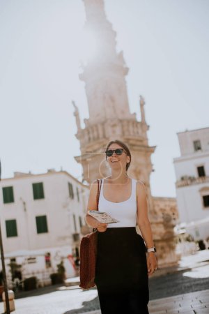 Foto de Turista femenina con un mapa de la ciudad junto a la estatua de Saint Oronzo en Ostuni, Italia - Imagen libre de derechos