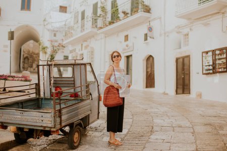 Téléchargez les photos : Touriste féminine avec une carte de ville en papier sur les rues étroites de Ostuni, Italie - en image libre de droit