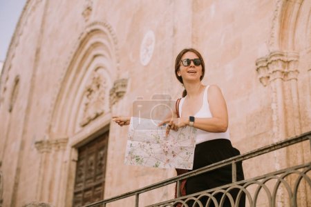 Foto de Turista femenina con un mapa de la ciudad por la iglesia San Francesco d 'Assisi en Ostuni, Italia - Imagen libre de derechos