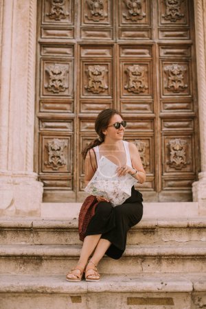 Téléchargez les photos : Touriste féminine avec une carte de la ville près de l'église San Francesco d'Assisi à Ostuni, Italie - en image libre de droit