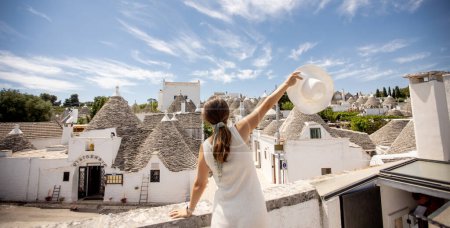 Téléchargez les photos : Une jeune femme en robe blanche et chapeau par une journée ensoleillée lors d'une visite touristique à Alberobello, Italie - en image libre de droit