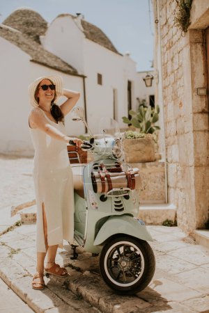 Foto de Una joven con un vestido blanco y sombrero en un día soleado durante la visita turística en Alberobello, Italia - Imagen libre de derechos