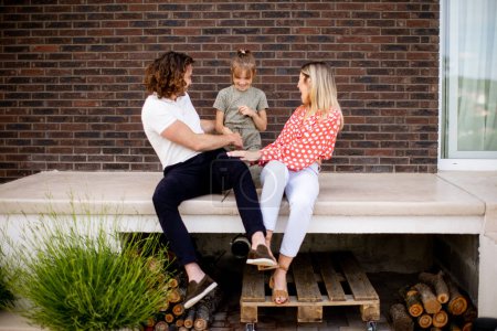 Photo for Family with a mother, father and daughter sitting outside on steps of a front porch of a brick house - Royalty Free Image