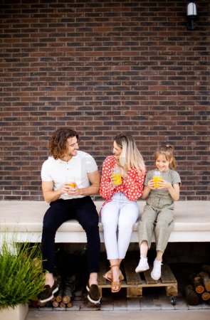 Téléchargez les photos : Famille avec une mère, un père et une fille assis dehors sur les marches d'un porche d'une maison en brique - en image libre de droit