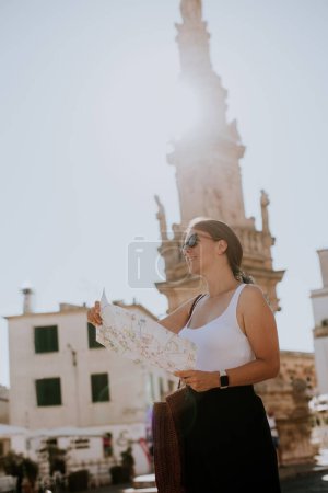 Foto de Turista femenina con un mapa de la ciudad junto a la estatua de Saint Oronzo en Ostuni, Italia - Imagen libre de derechos